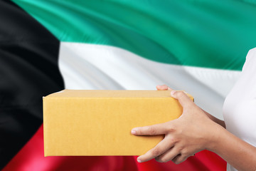 Kuwait delivery service. International shipment theme. Woman courier hand holding brown box isolated on national flag background.