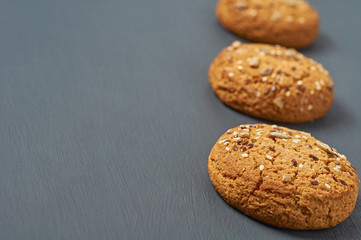 Row of three fresh homemade cookies with seeds of sunflower and sesame lies on dark scratched concrete table on kitchen. Space for text