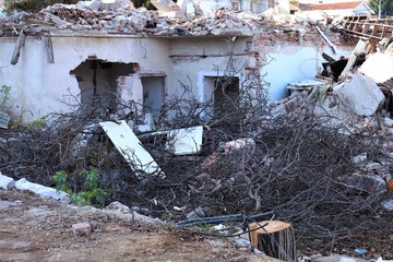 An old abandoned house without windows and doors with a pile of construction debris and branches in...