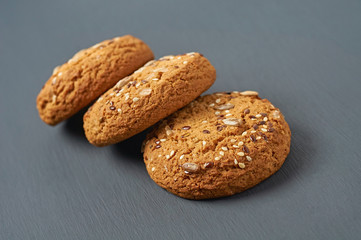 Row of three fresh homemade cookies with seeds of sunflower and sesame lies on dark scratched concrete table on kitchen. Close-up