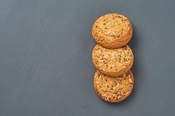 Row of three fresh homemade cookies with seeds of sunflower and sesame lies on dark scratched concrete table on kitchen. Space for text. Top view