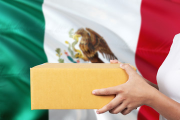 Mexico delivery service. International shipment theme. Woman courier hand holding brown box isolated on national flag background.
