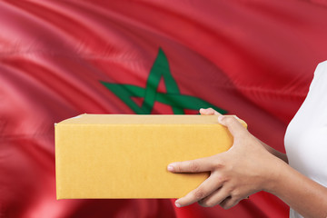 Morocco delivery service. International shipment theme. Woman courier hand holding brown box isolated on national flag background.