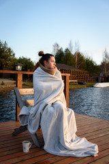 A young girl in a warm plaid rests by the lake in autumn. The concept of enjoying nature, relaxation, travel