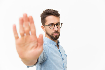 Serious strict guy making hand stop gesture. Handsome young man in casual shirt and glasses...