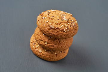 Heap of three fresh homemade cookies with seeds of sunflower and sesame lies on dark scratched concrete table on kitchen. Close-up