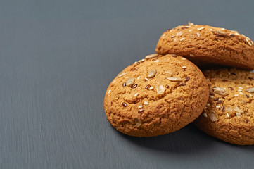 Heap of three fresh homemade cookies with seeds of sunflower and sesame lies on dark scratched concrete table on kitchen. Space for text