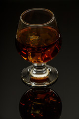Whiskey with ice or brandy in a glass on a glass reflective surface. Whiskey with ice in a glass. Whiskey or brandy. Selective focus.