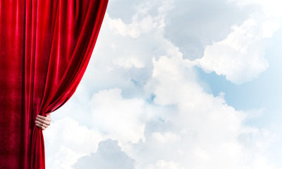 Cloudy landscape behind red curtain and hand holding it