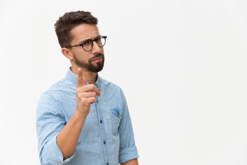 Frowning concerned guy shaking finger at camera. Handsome young man in casual shirt and glasses...