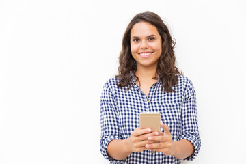 Happy joyful female customer holding cell and looking at camera. Young woman in casual checkered...