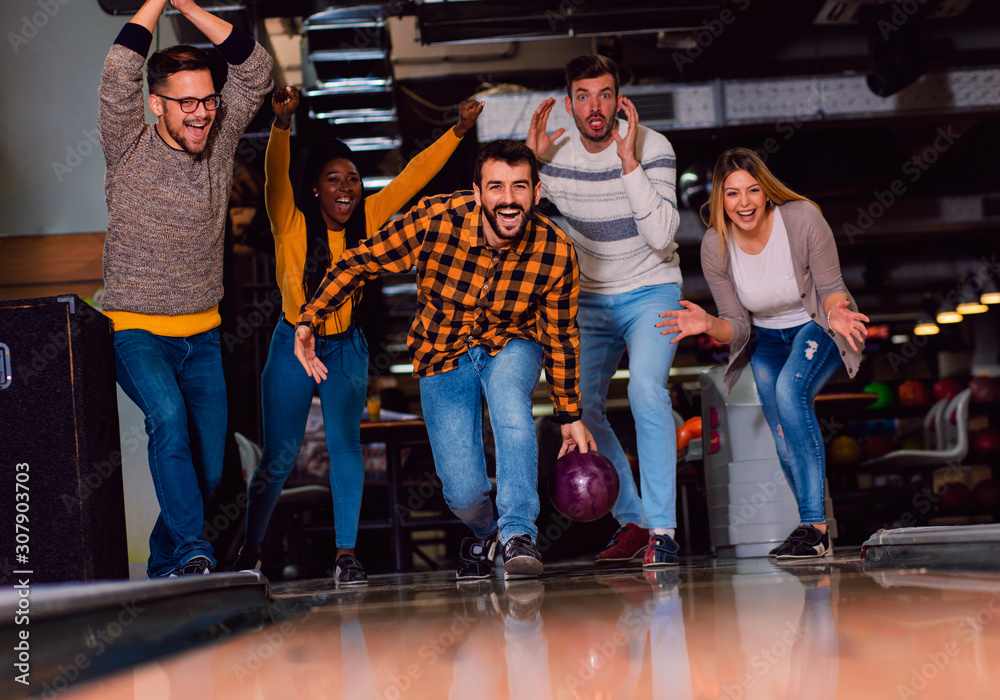 Wall mural Group of friends enjoying time together laughing and cheering while bowling at club.