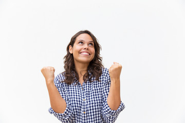 Obraz na płótnie Canvas Cheerful happy woman making winner gesture and looking up at copy space. Young woman in casual checked shirt standing isolated over white background. Great news concept
