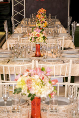 Elegant white table for dinner, with glass cups and vases with roses. With Plates