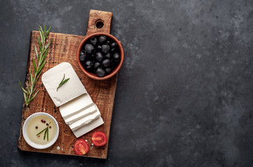 feta cheese, with rosemary, tomatoes, olives on a stone background. top view with copy space for...