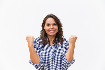 Joyful excited woman making winner gesture, celebrating success or good news. Young woman in casual checked shirt standing isolated over white background. Luck concept