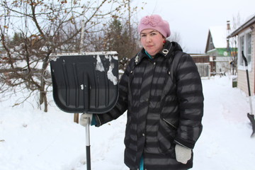 a woman shovels snow in the yard of a rural house.time of year winter.it's freezing outside.