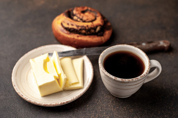 coffee and a bun with poppy seeds, butter and a knife on a stone background. breakfast concept with copy space for your text
