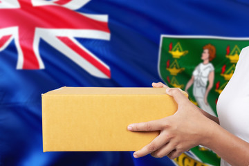 British Virgin Islands delivery service. International shipment theme. Woman courier hand holding brown box isolated on national flag background.
