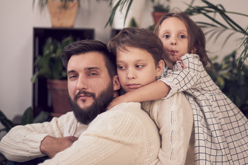 Fototapeta premium Two young children kissing their father while home