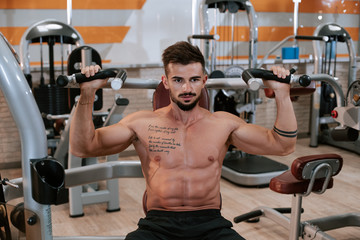 Shirtless muscular young man doing barbell bench press exercise at the gym