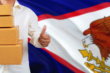American Samoa real estate sale concept. Wooden house model with discount tag on national flag...
