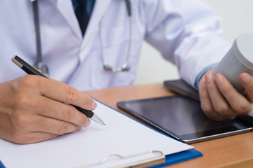 Fototapeta premium Doctor holding bottle of pills and writing prescription