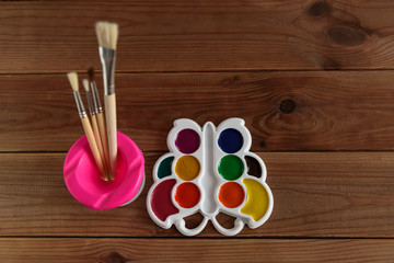 Set of colorful dry watercolor paints in a white plastic palette and brushes on a wooden table.