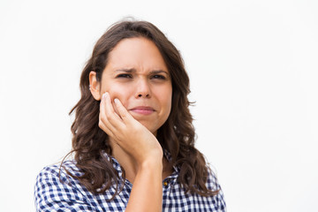 Closeup of stressed Latin woman holding cheek. Young woman in casual checked shirt standing isolated over white background. Thinking, or toothache concept