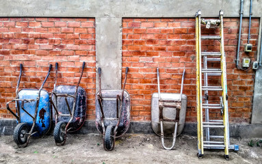 Old construction wheelbarrows crouched on orange wall next to yellow staircase.