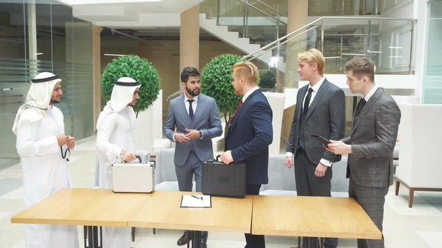 Translator between businessmen, sheikh and caucasian. Sheikh holding white case, caucasian black case. Translator of arabic and english languages