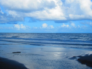 Le soleil couchant et les nuage se reflètent dans la mer en bord de plage