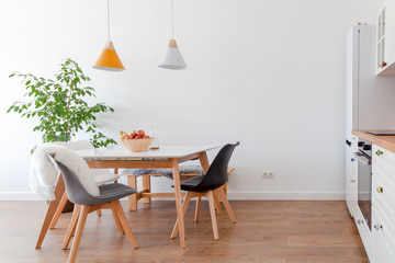 Modern interior of cozy kitchen, dining room, white furniture, lamps above wooden table, chairs,...