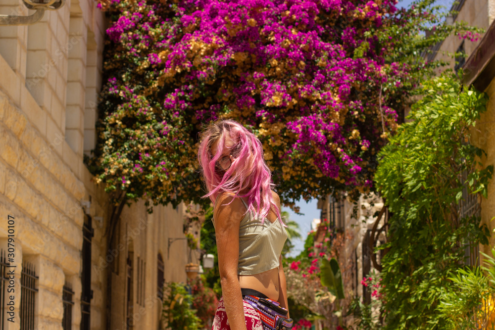 Wall mural young girl portrait with face behind pink hair in center of composition on old city street with rose