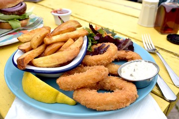  Fried calamari with salad and potato chips on blue ceramic plate and yellow table background.