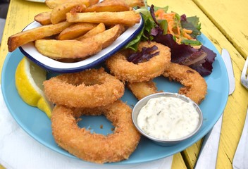  Fried calamari with salad and potato chips on blue ceramic plate and yellow table background.