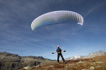 Paraglider Pilot stands on a slope and balances his paraglider above his head in the Alps of...