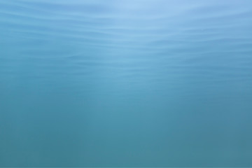 Picture of blue to green shades of water mass from under water. Fine structure of waves from below. Light blue to azure color transition.