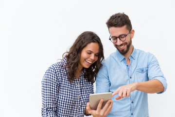Cheerful couple watching content on tablet and laughing. Young woman in casual and man in glasses...
