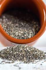 Edible seeds of chia, Salvia hispanica, a flowering plant of the mint family. A popular healthy food product. Chia seeds are poured from a brown clay pot. Blurred.