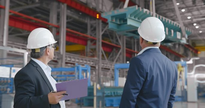 Construction engineers businessmen, teamwork meeting in plant facility. Two senior confident business people formal wear pointing to moving crane. investor businessman at modern factory