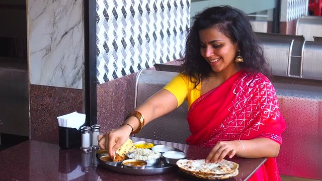 beautiful woman eating dosa chutney naan and indian tali in a restaurant.She wearing red sari with gold earrings , with tilaka on her forehead
