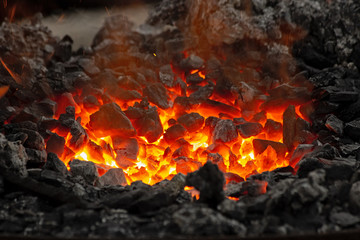 Flame and embers glow in a bonfire. Fire, heat, coal and ash with flying sparks.
