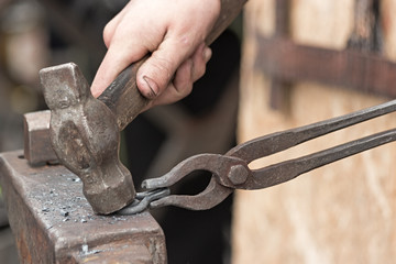 The blacksmith makes an iron loop with a hammer and tongs, forging on the anvil.