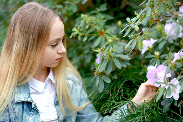 young girl with long white hair in a denim jacket walks in the garden with blooming azalea