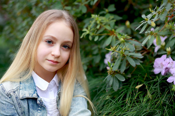 young girl with long white hair in a denim jacket walks in the garden with blooming azalea