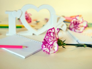 Fresh pink carnations, the word love from volume letters, hearts, blank notebooks, paper, pencils on a light background, top view, getting ready to congratulate mom