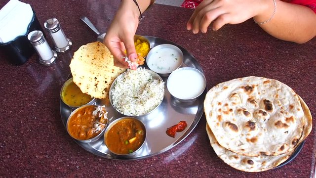 close up cropped hands of beautiful woman eating dosa chutney naan and indian tali in a restaurant