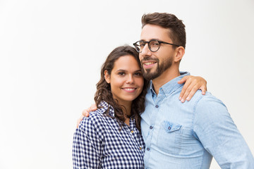 Positive beautiful couple hugging and looking at camera. Young woman in casual and man in glasses posing isolated over white background. Affection concept
