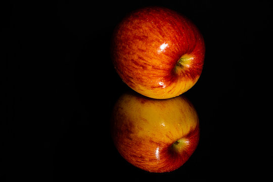 A low key image of a single golden and red apple on it's side on a highly reflective surface against a black background with plenty of room for copy.